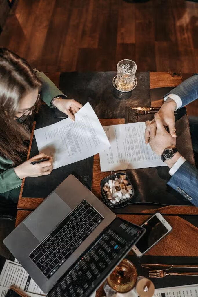 High angle shot of a business meeting with a woman signing a contract on a table with a laptop.